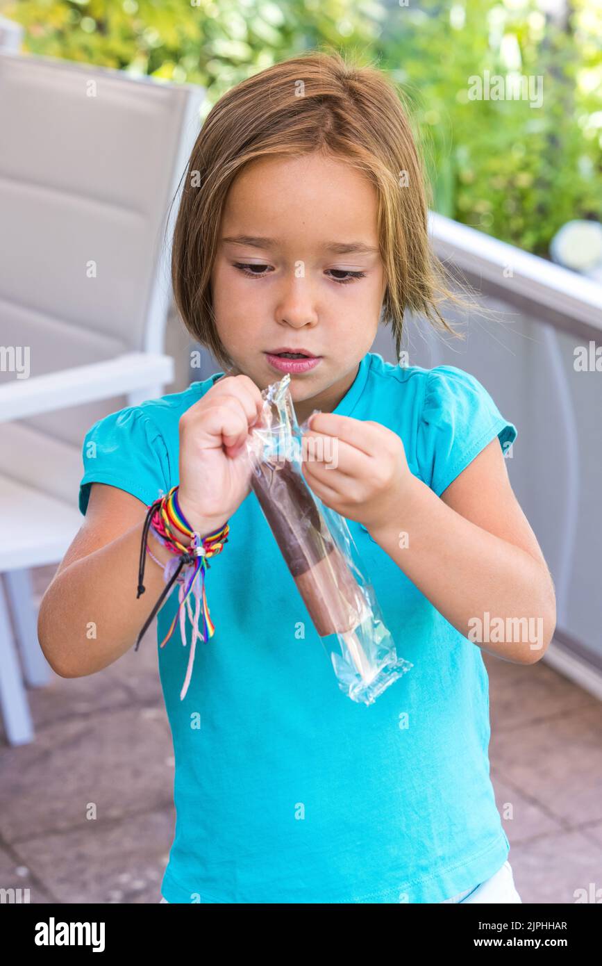 Fille portant un t-shirt vert, tenant une glace au chocolat au lait, dans la rue, en été, en prenant le plastique. Crème glacée, popsicle, manger, sucré Banque D'Images