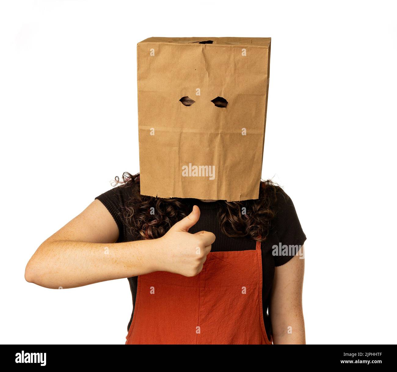 Jeune femme portant un sac en papier sur sa tête avec les pouces vers le haut pour approbation Banque D'Images