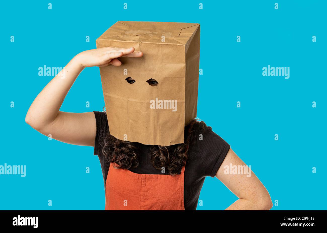 Femme portant un sac en papier au-dessus de sa tête regardant autour Banque D'Images