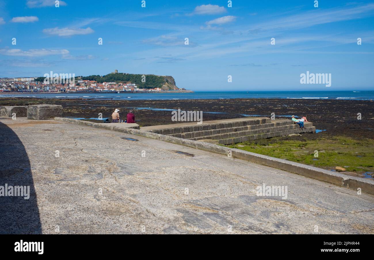 Couples plus âgés assis sur une digue avec le château de Scarborough et la vieille ville en arrière-plan Banque D'Images