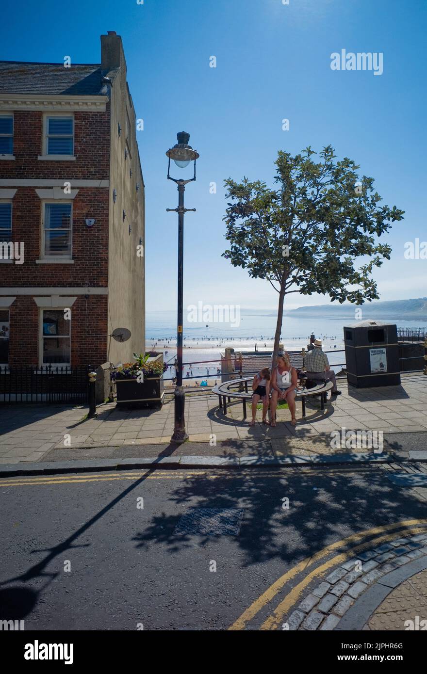 Scène de rue à Eastborough, Scarborough lors d'une journée chaude avec siège d'arbre et la plage derrière Banque D'Images