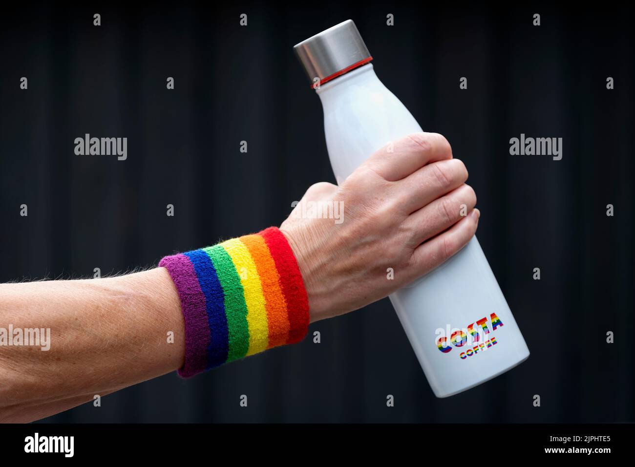 Une femme d'âge moyen portant un bandeau anti-transpiration gay Pride autour de son poignet. Elle tient une bouteille de boissons portant le logo costa Coffee dans des couleurs de fierté gay Banque D'Images