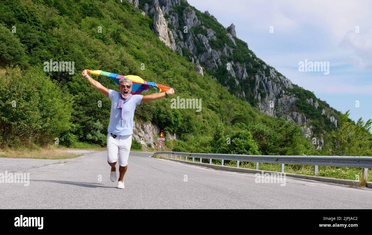 Portrait d'un homme caucasien âgé âgé âgé à cheveux gris bisexualité avec une barbe et des lunettes de soleil portant un drapeau arc-en-ciel LGBTQIA sur la nature. Célèbre le mois de la fierté, le Rainbow Flag Day, la parade des gays Banque D'Images