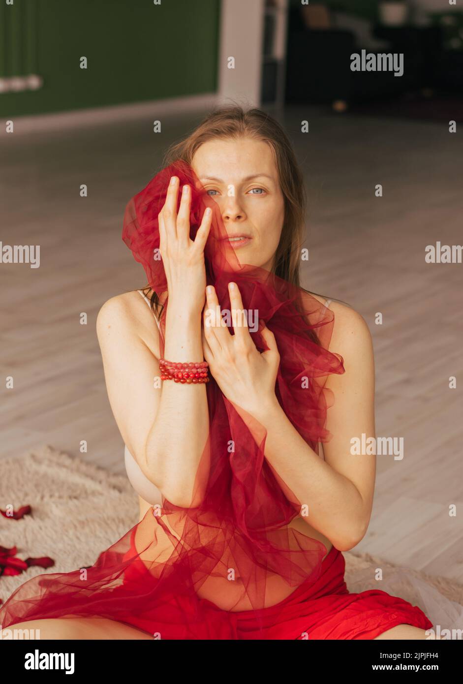 Femme aux cheveux longs blonds et un tissu rouge transparent dans ses mains, portrait Banque D'Images