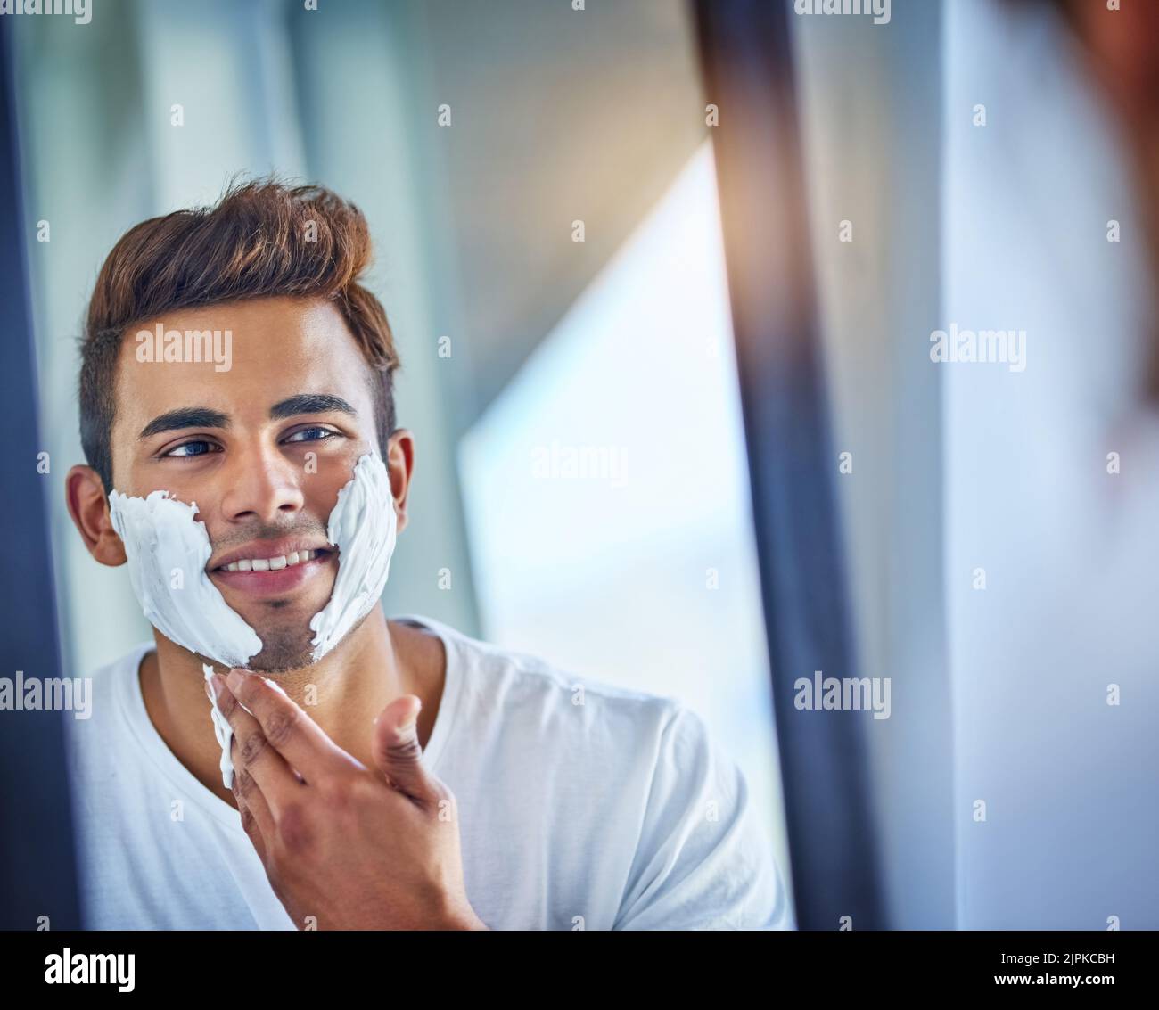 Toilettage pour s'assurer qu'il donne sa meilleure première impression. Un beau jeune homme se rasant ses cheveux faciaux dans la salle de bains. Banque D'Images