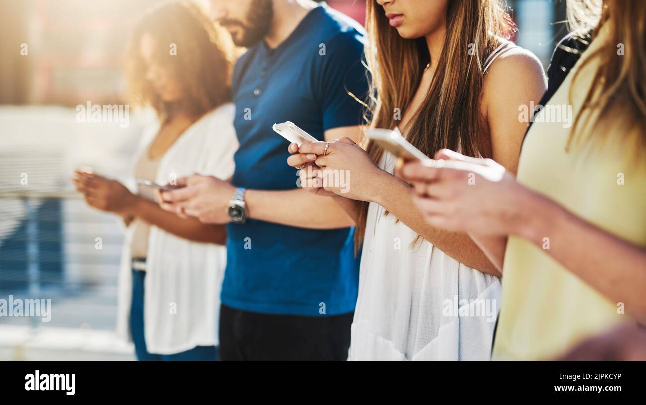 Un groupe de jeunes gens méconnaissables qui envoient des SMS sur leur téléphone portable tout en étant debout à l'extérieur. Banque D'Images