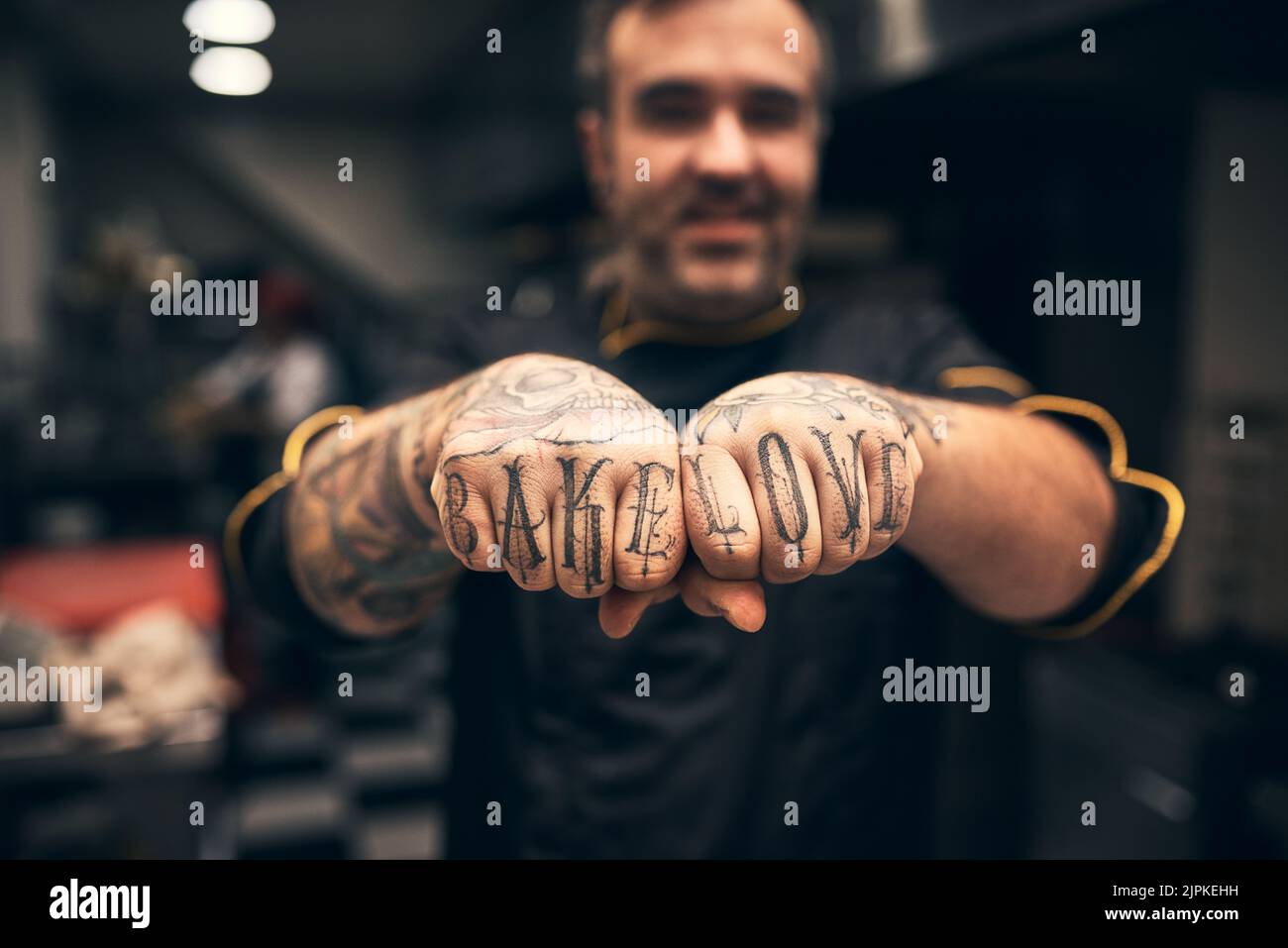 J'adore la pâtisserie. Un jeune chef joyeux tenant ses poings à l'appareil photo avec les mots tatoués sur eux Bake Love. Banque D'Images