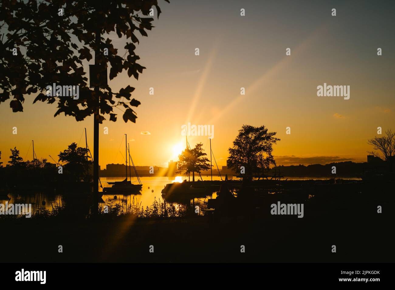 Des rayons de soleil dorés au coucher du soleil sur le port de Boston avec des bateaux et des arbres Banque D'Images