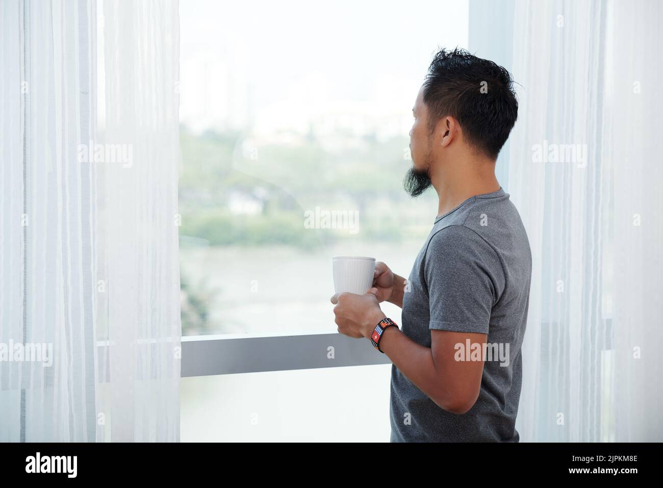 Homme buvant son café du matin et regardant par la fenêtre Banque D'Images