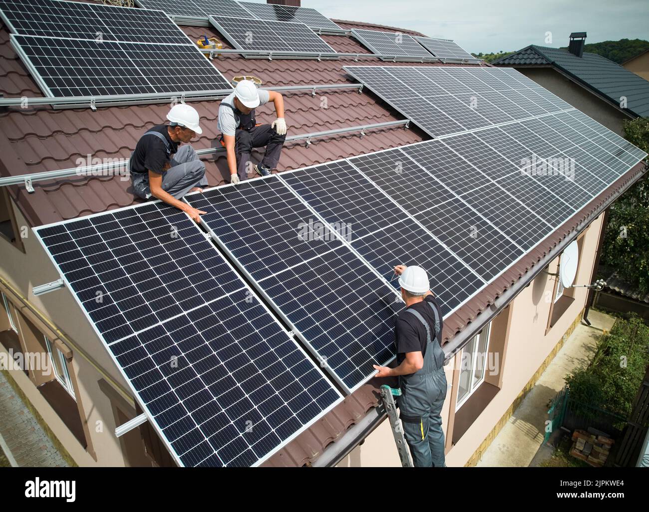 Hommes installateurs montage de modules solaires photovoltaïques sur le toit de la maison. Ingénieurs en casques installant un système de panneaux solaires à l'extérieur. Concept d'énergie alternative et renouvelable. Vue aérienne. Banque D'Images