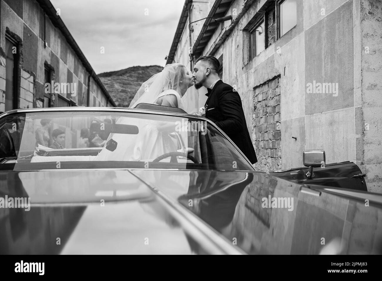 Photo en niveaux de gris d'un couple caucasien embrassant dans une voiture d'époque pendant le mariage Banque D'Images