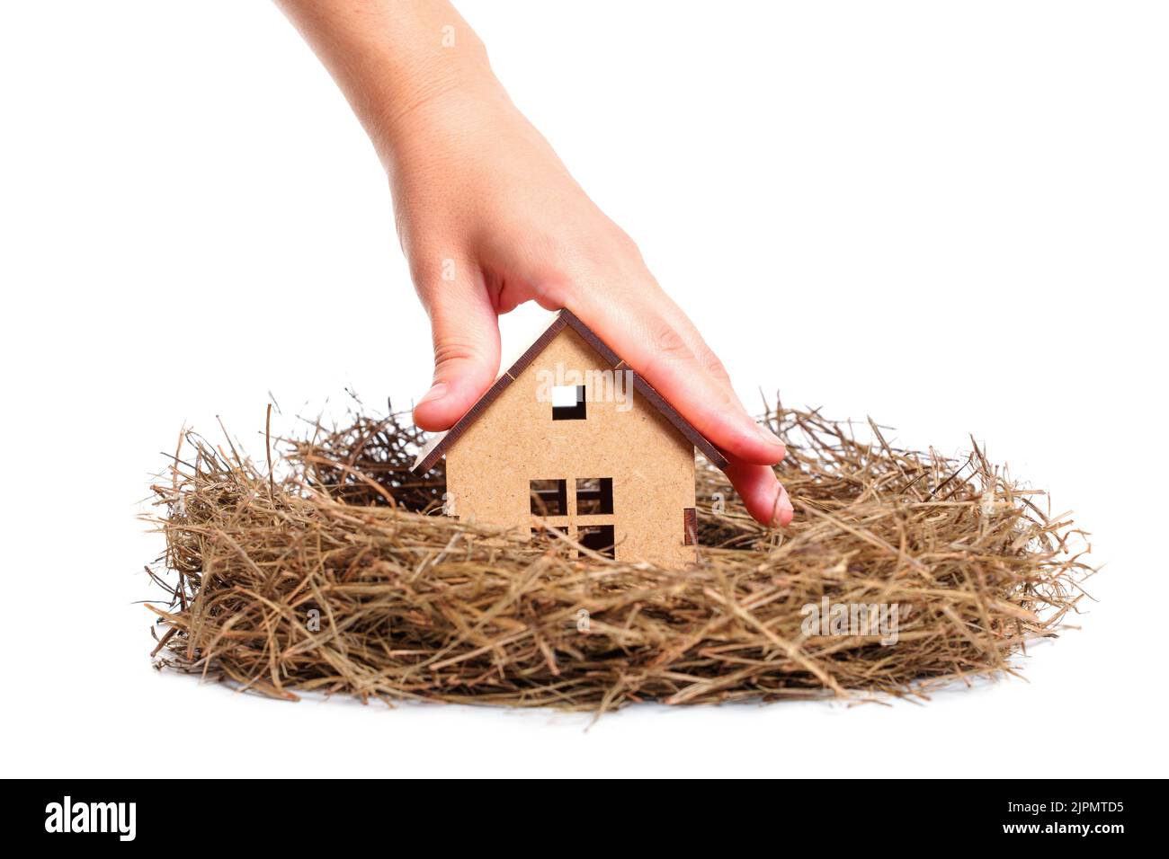 Main plaçant une maison en bois miniature dans un nid de foin isolé sur fond blanc. Concept de maison familiale. Banque D'Images