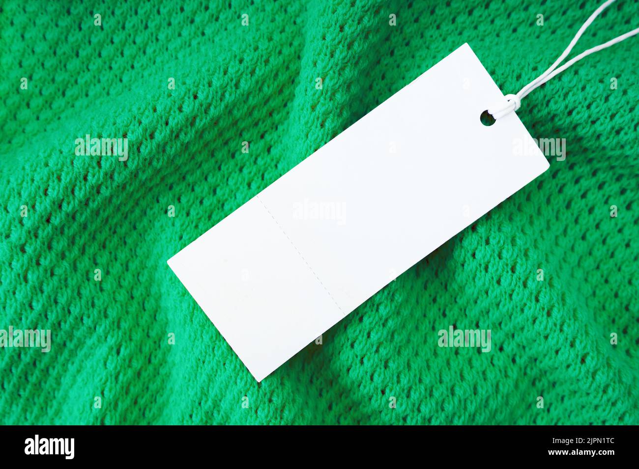 Blanc blanc vierge rectangulaire étiquette de vêtement, modèle de maquette d'étiquette sur fond de tissu tricoté vert . Étiquette de prix avec espace pour le texte. Shopping, s Banque D'Images