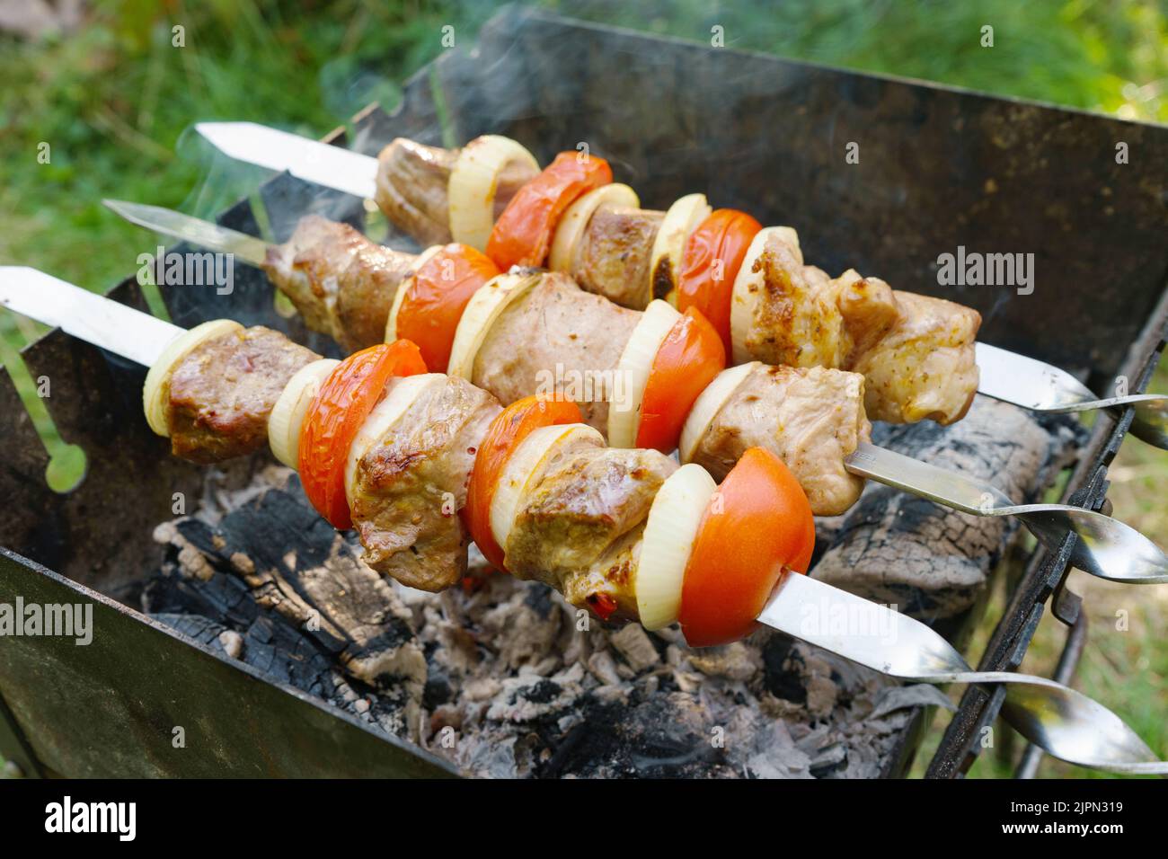 Morceaux de viande marinés à la tomate et à l'oignon sur des brochettes de métal cockées sur un barbecue au charbon de bois. Kebab grillé au charbon de bois. Banque D'Images