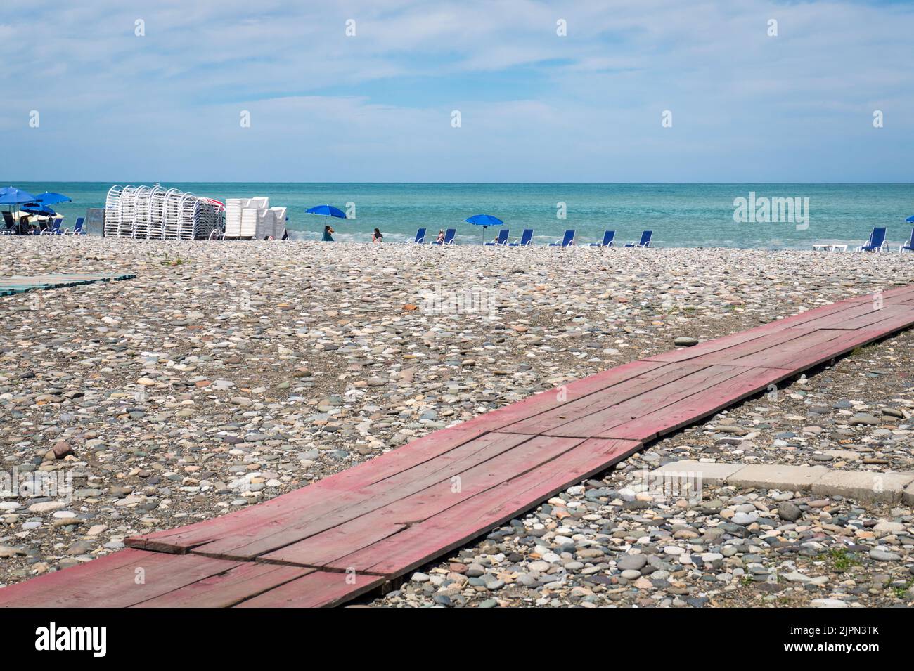 Plage de Batumi, Géorgie. Un chemin en bois sur une plage de galets. Lumineux été jour ensoleillé, eau bleue. Banque D'Images