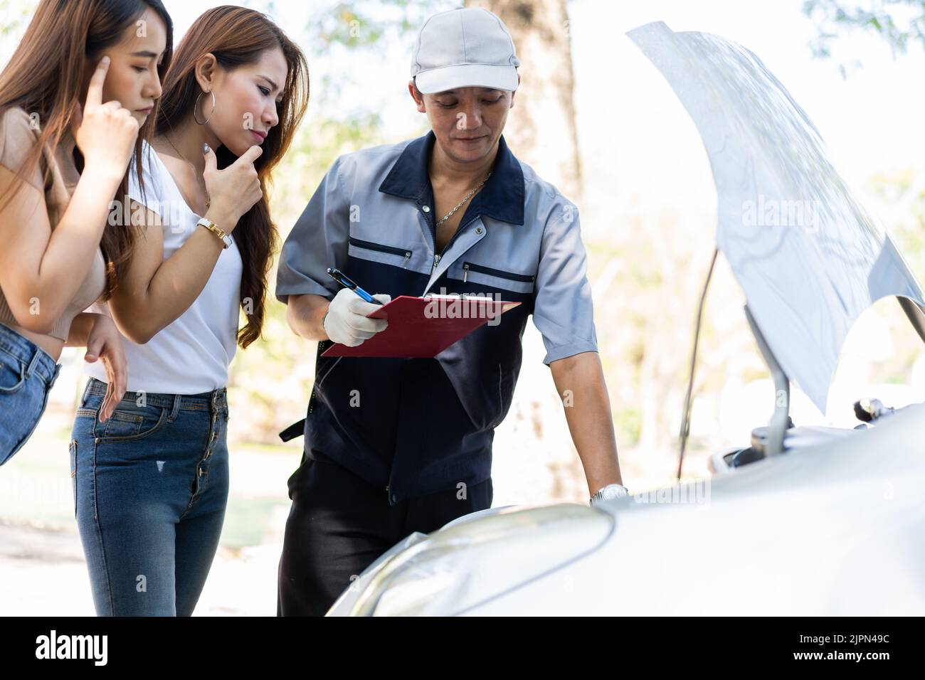 Le mécanicien automobile asiatique mâle tient un presse-papiers et examine le problème de panne de moteur de voiture avec les femmes client et d'expliquer la cause racine et d'estimer repari Banque D'Images