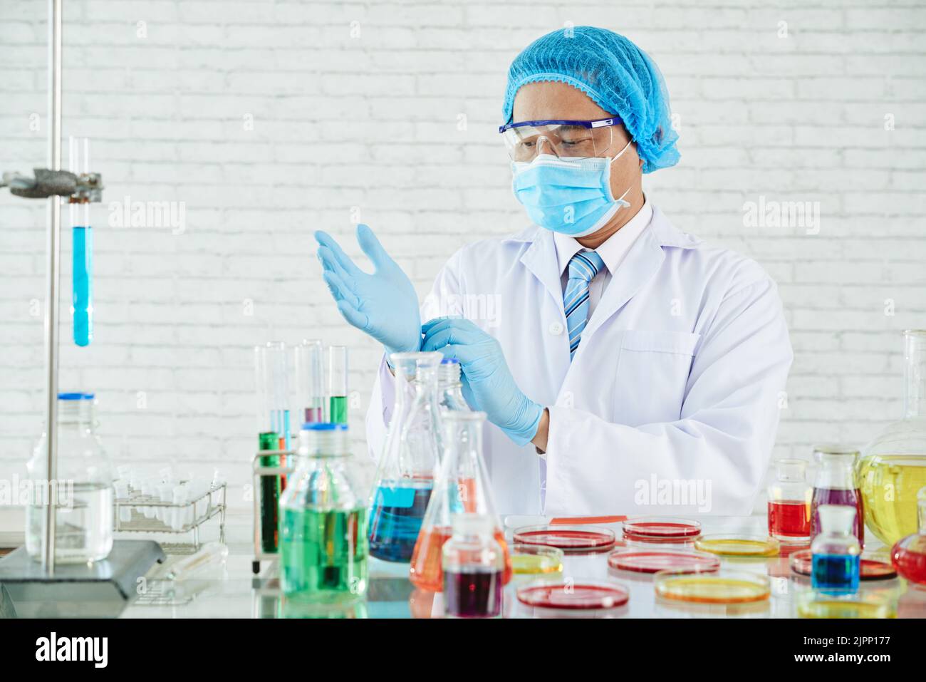 Portrait à la taille haute d'un scientifique hautement professionnel portant des gants en caoutchouc à revêtement blanc réglable tout en étant debout sur une paillasse de laboratoire Banque D'Images