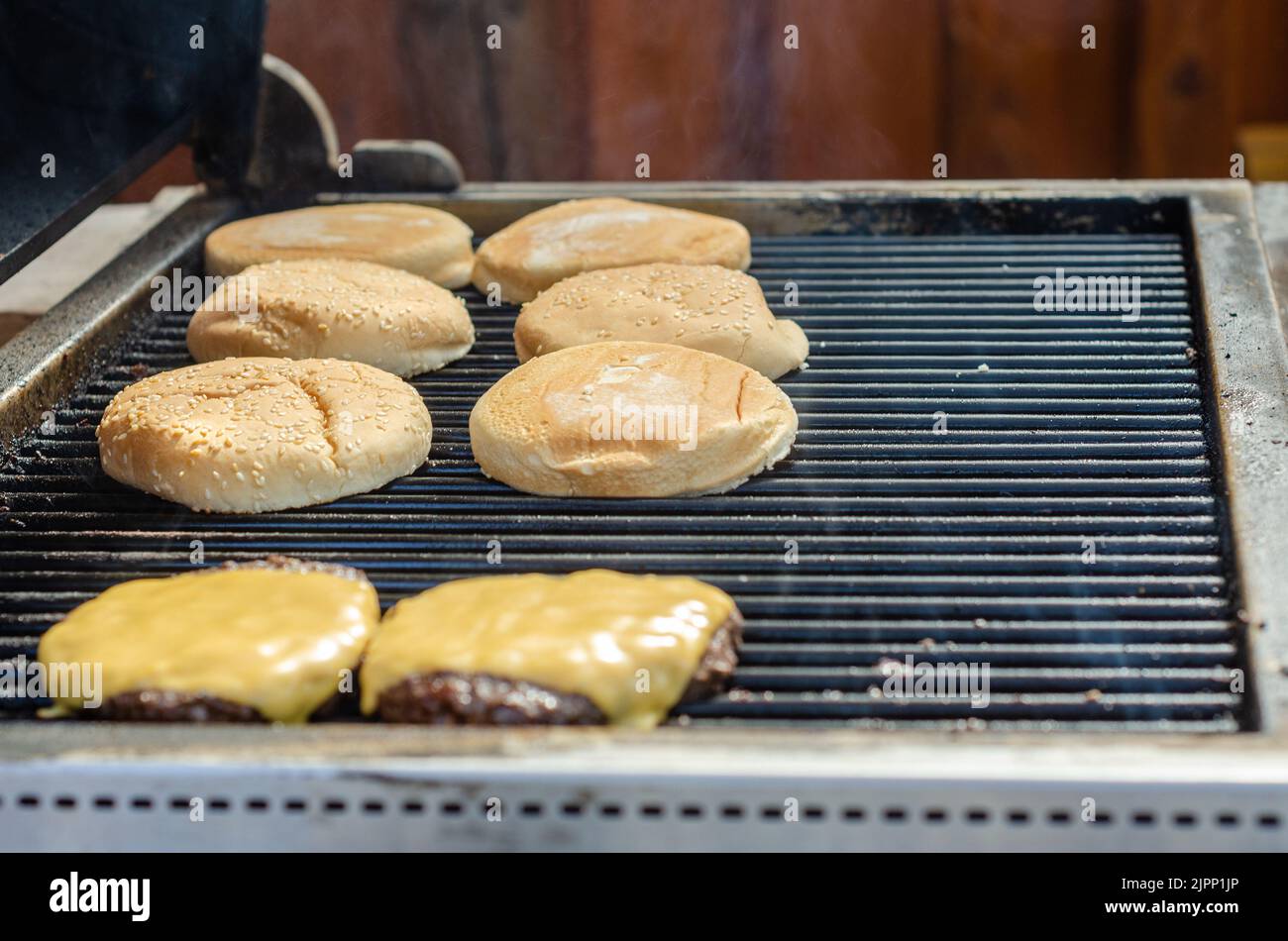 Les petits pains hamburger grillent légèrement et fondent le fromage sur un barbecue prêt à assembler un cheeseburger fini. Banque D'Images