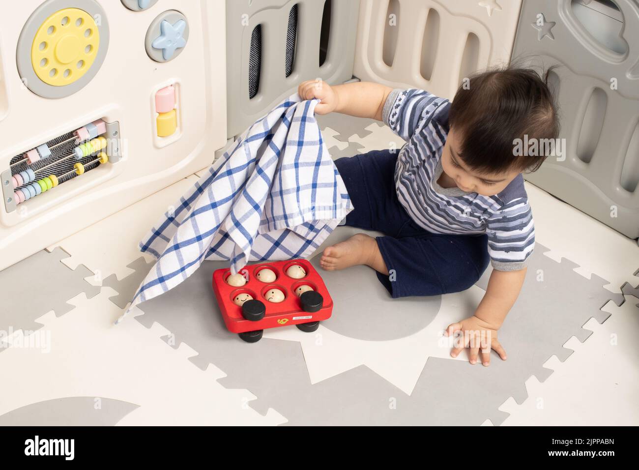 Bébé garçon de 11 mois à la maison soulever le tissu pour trouver le jouet caché Piaget objet permanence série #2 Banque D'Images