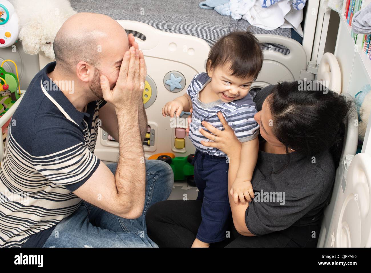 bébé garçon de 11 mois à la maison avec les parents bébé se tournant pour rire avec la mère comme le père joue un coup de piquer Banque D'Images