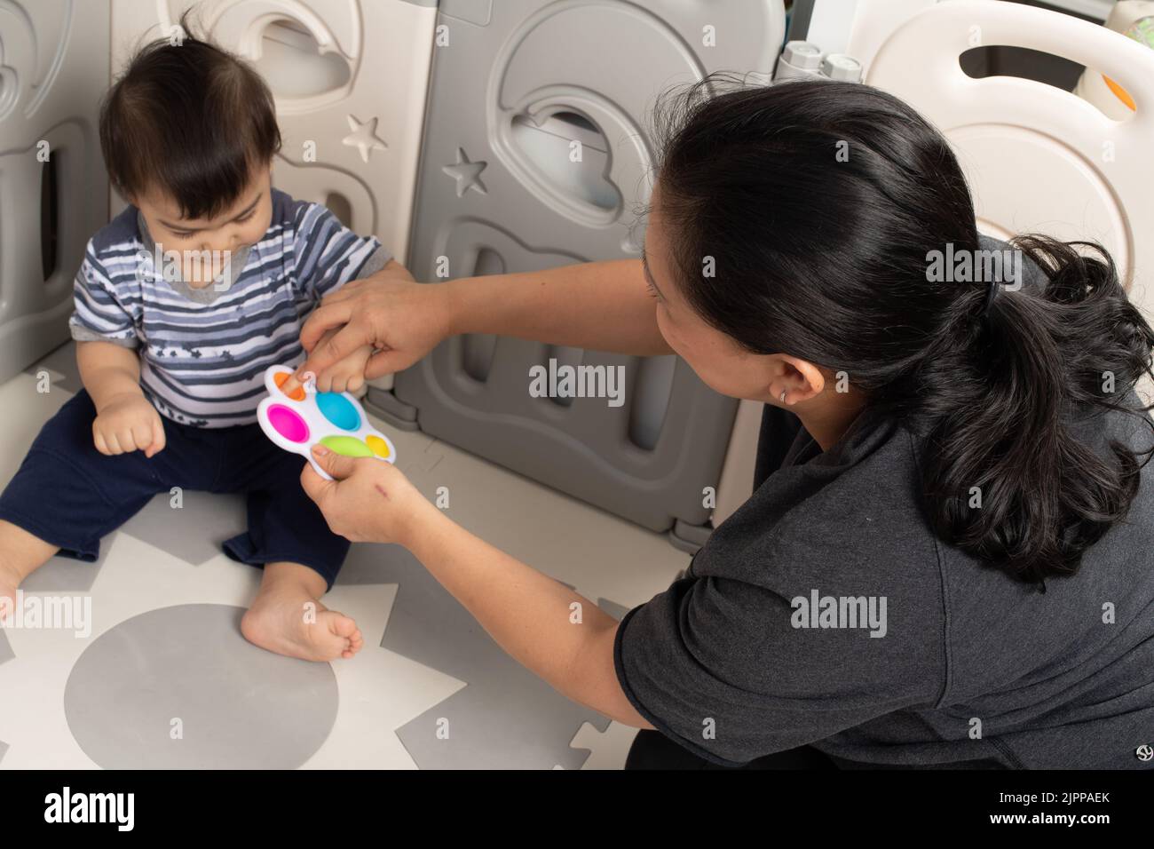 bébé garçon de 11 mois à la maison avec une mère intéressée comme elle utilise son doigt pour presser nouveau jouet, lui montrant comment ça fonctionne Banque D'Images
