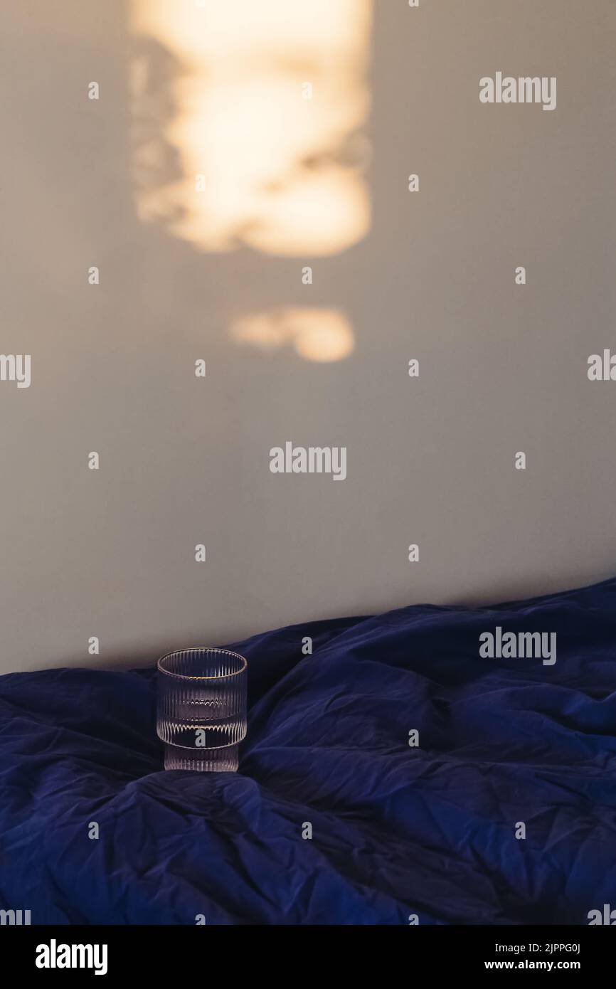 Verre d'eau dans le lit et lumière du soleil sur le mur de wight. Début de matinée, concept de style de vie minimaliste Banque D'Images