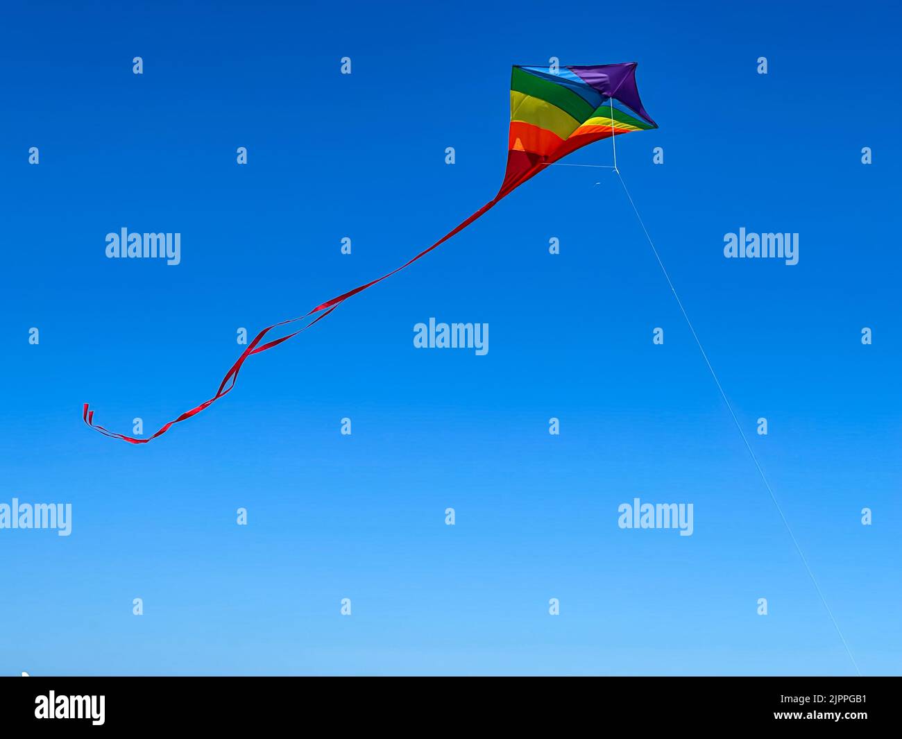 Un cerf-volant de couleur arc-en-ciel s'élève contre un ciel bleu de cobalt lors d'une journée ensoleillée au sud de la Floride. Banque D'Images