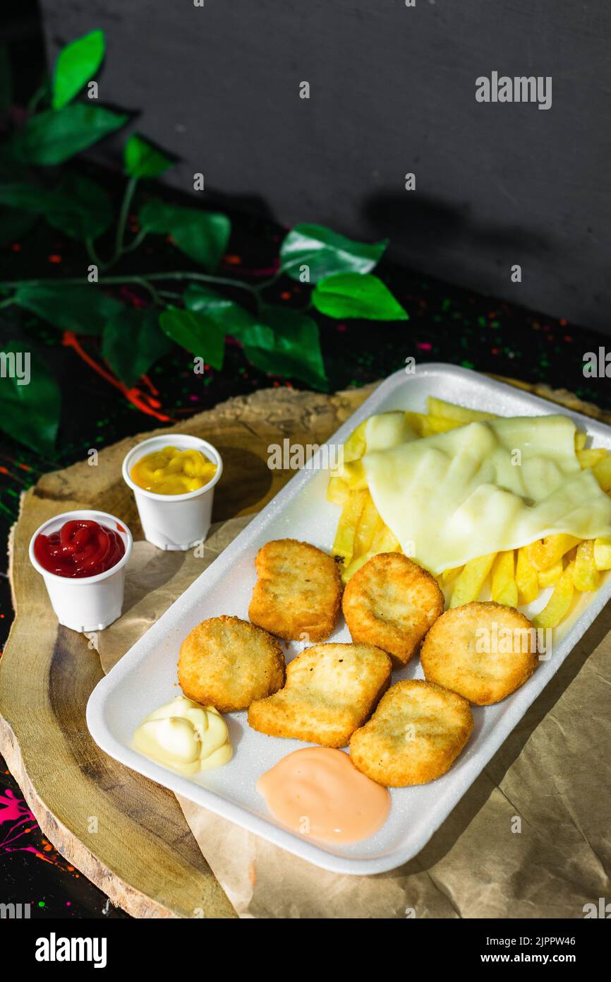 gros plan d'une assiette de nuggets de poulet avec pommes de terre et fromage mozzarella, servi sur un plateau en bois avec deux petits verres de sauce. noir Banque D'Images