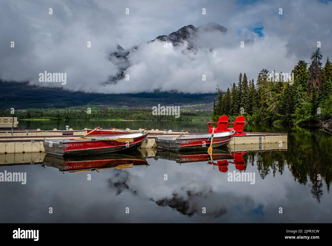 Des nuages bas un matin encore au lac Pyramid, quai du parc national Jasper avec des bateaux et des chaises rouges Banque D'Images