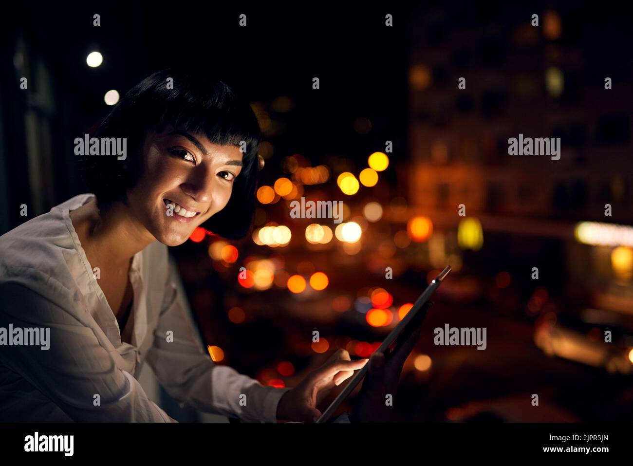 Vivre dans la ville signifie rester à jour. Une jeune femme attrayante utilisant une tablette numérique à l'extérieur de la ville la nuit. Banque D'Images