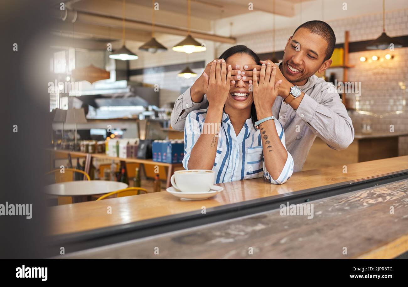 Ouah, surprise et romantique petit ami couvrant ses amies yeux pour un cadeau dans un restaurant, café-restaurant ou café-restaurant. Un cadeau d'anniversaire à Banque D'Images