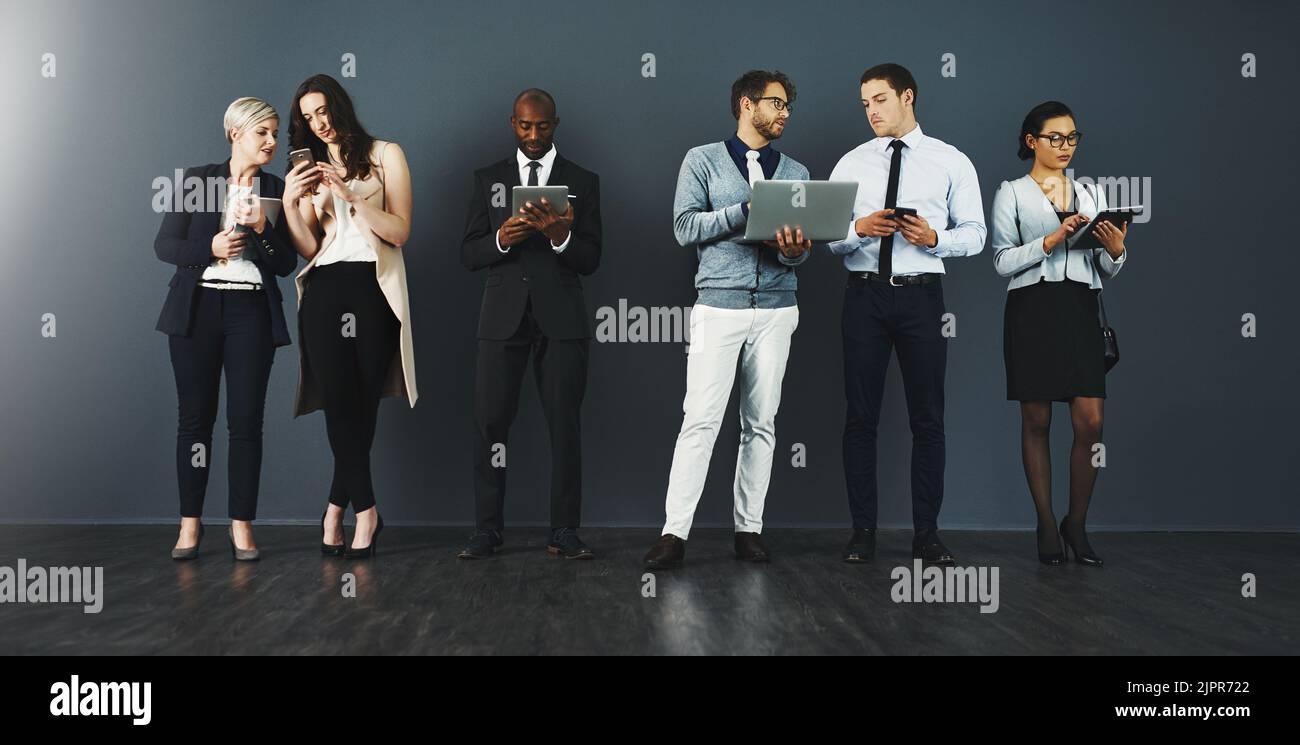 Rester productif grâce aux connexions sans fil. Photo en studio d'un groupe d'hommes d'affaires utilisant divers appareils numériques sur fond gris. Banque D'Images