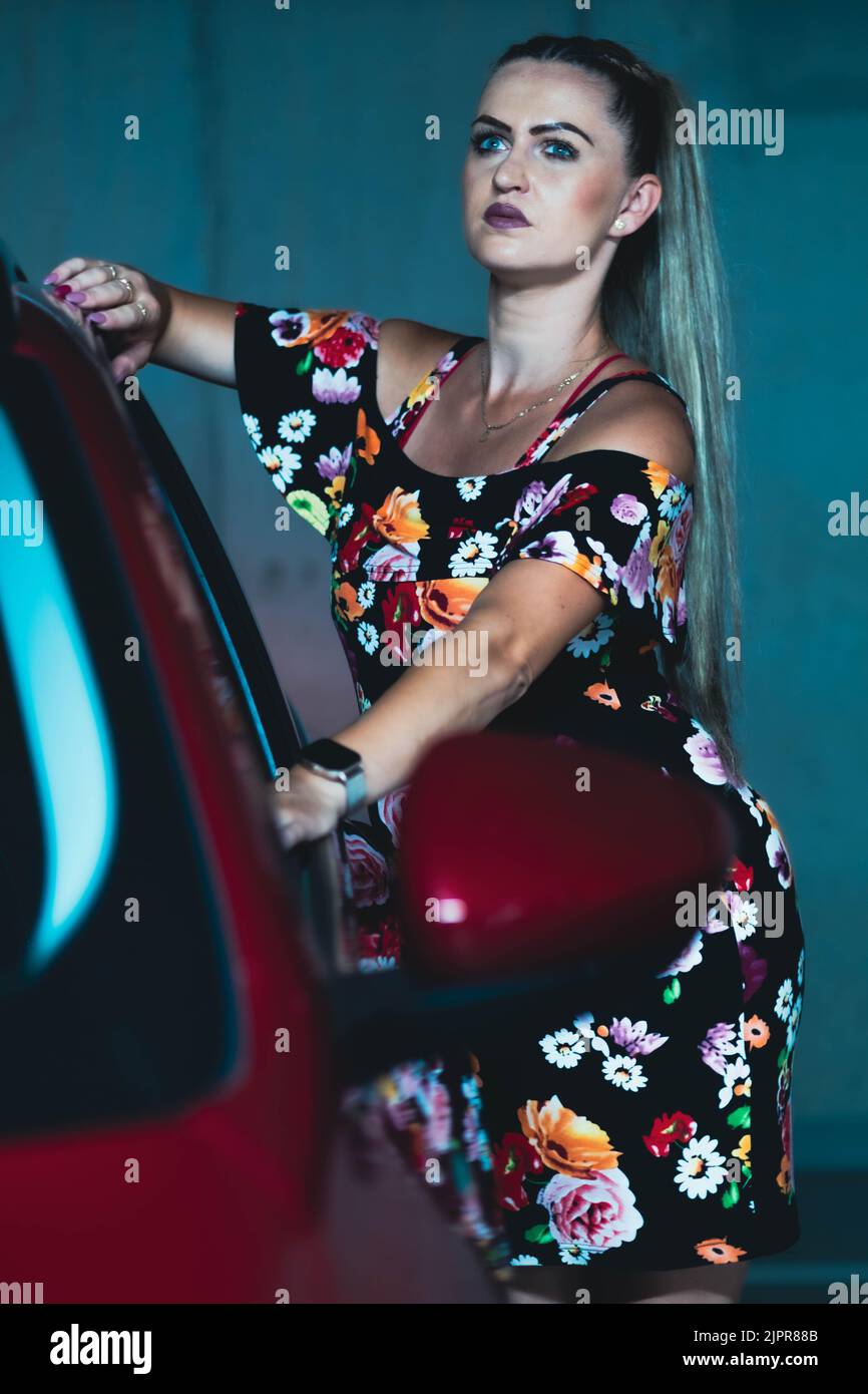 Belle dame pochant avec le tipo de fiat rouge dans un garage sombre avec des lumières de cinéma Banque D'Images