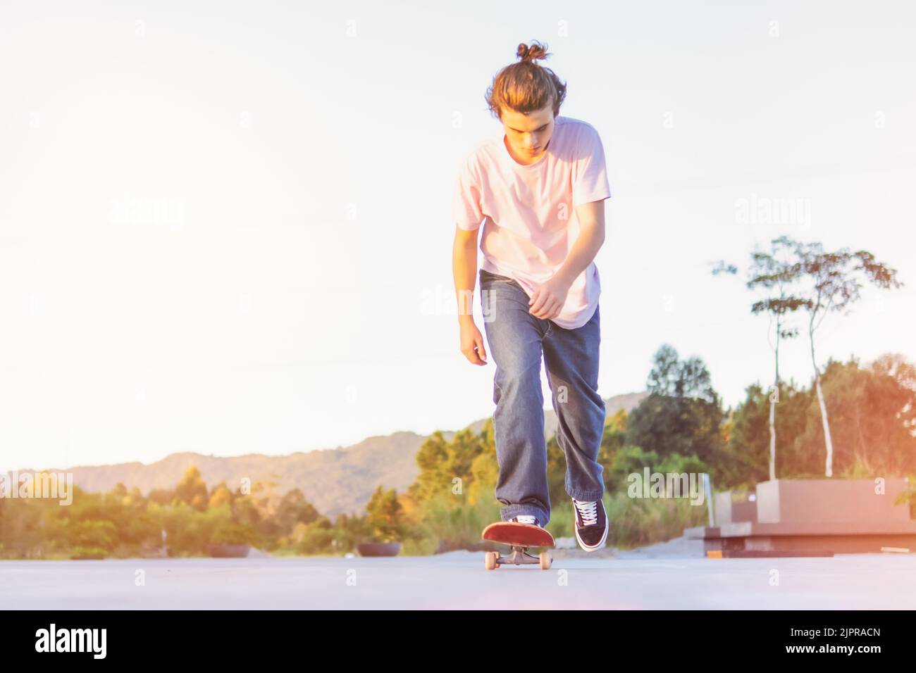 Jeune skateur sautant et effectuant un tour sur une route désertique asphaltée isolée sur le ciel au coucher du soleil - patineur adolescent pratique un skateboard dehors Banque D'Images