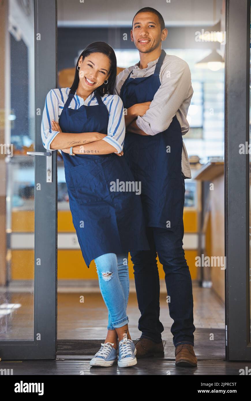 Les propriétaires de petites entreprises se tenant à l'entrée de leur café-restaurant, fiers et prêts pour le client. Un jeune couple de puissance enthousiaste à l'idée de sa mise en route Banque D'Images