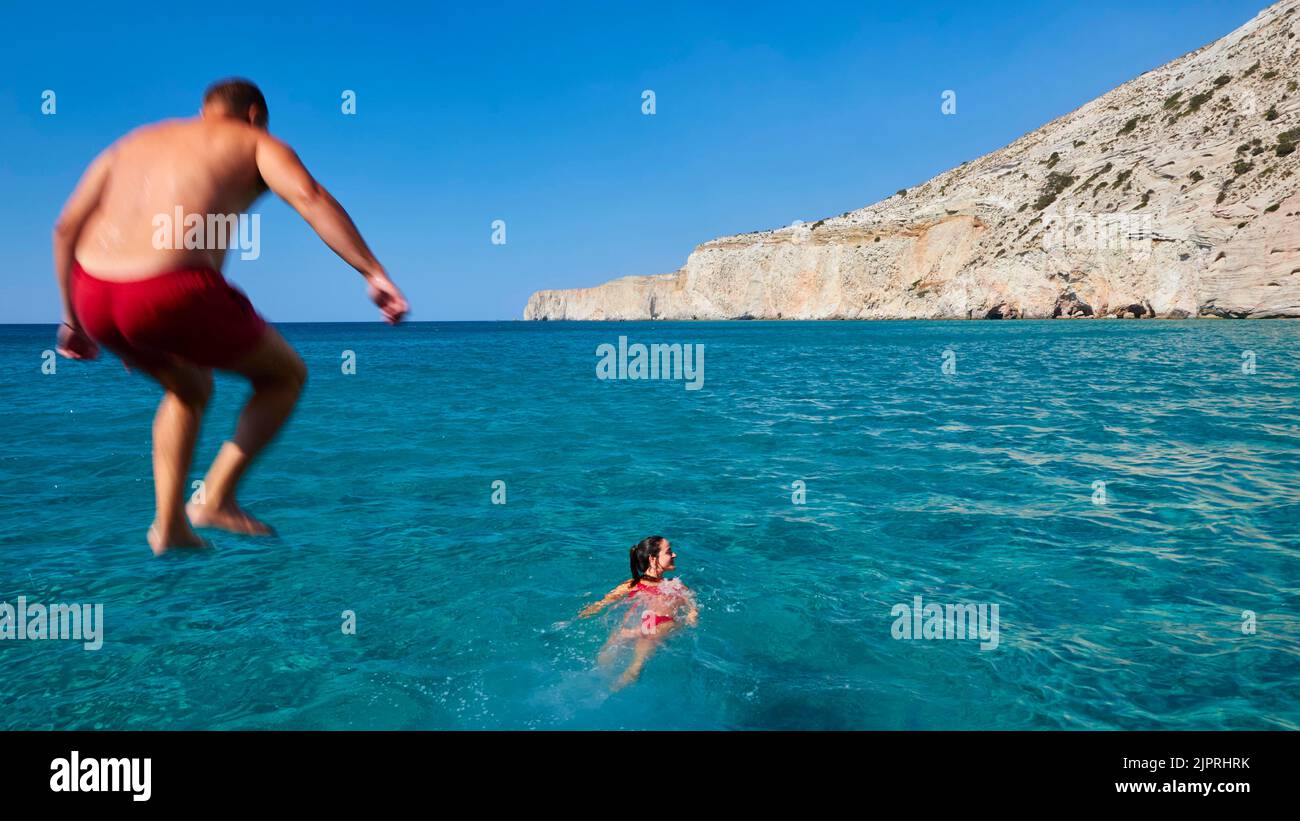Voyage en bateau, homme en maillot de bain rouge saute du bateau à la mer, femme en bikini rouge nains devant le bateau, grottes, Kleftiko, formations tuff, turquoise de mer Banque D'Images