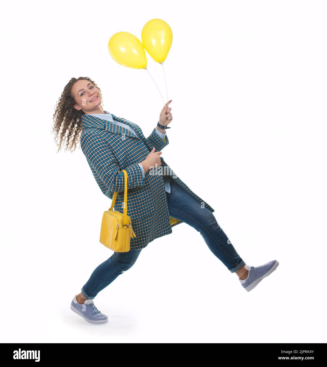 Belle jeune fille dans un manteau léger avec un sac jaune marche avec des ballons jaunes Banque D'Images