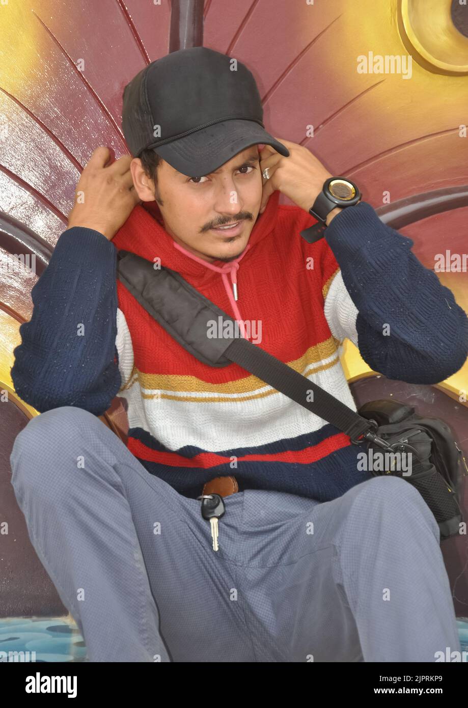 Vue avant d'un jeune homme regardant l'appareil photo tout en ajustant le sweat à capuche pendant qu'il est assis Banque D'Images