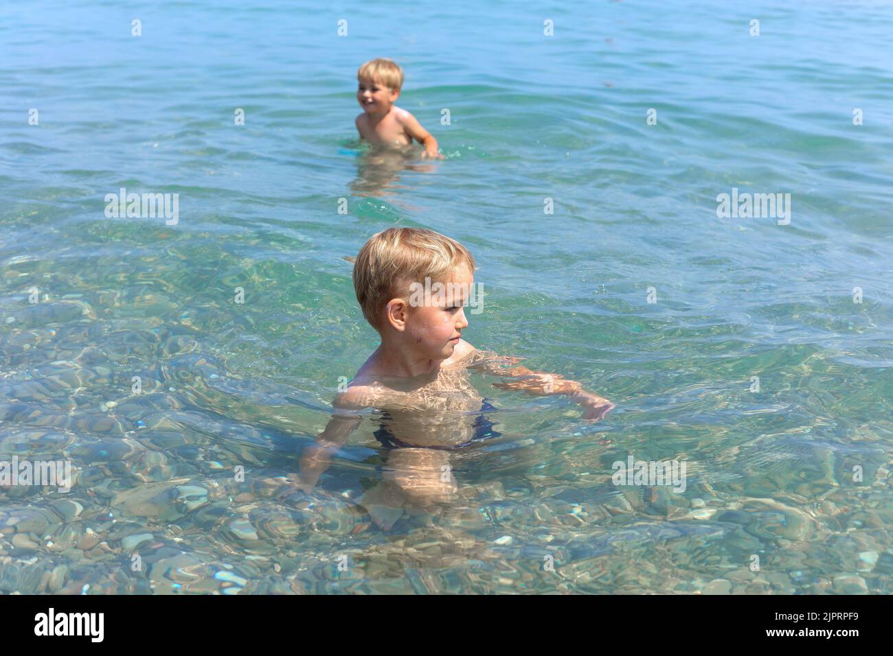 Un petit garçon souriant se détend sous le soleil d'été dans des eaux de mer peu profondes. Concept de vacances d'été en famille. Banque D'Images