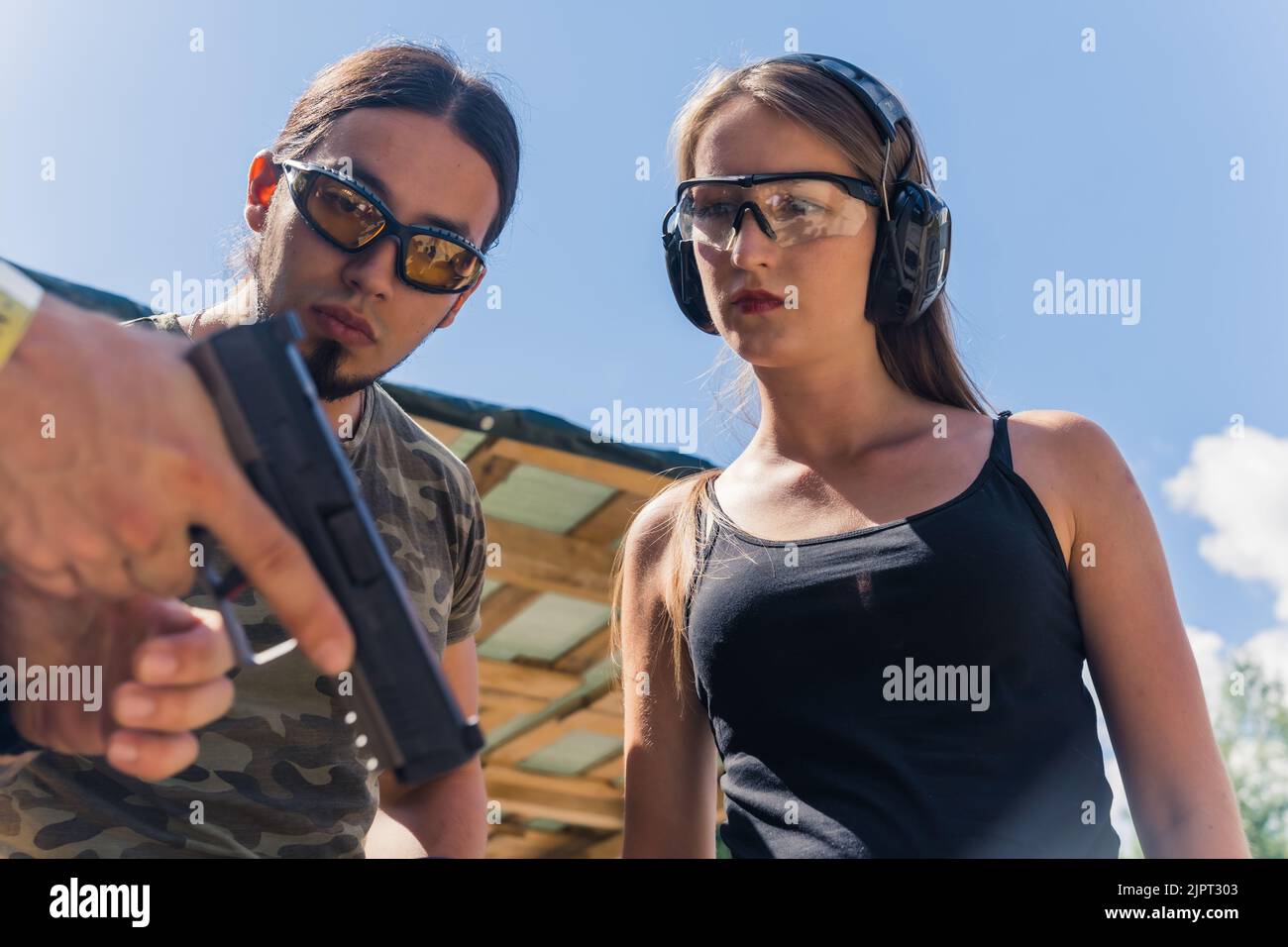 Homme et femme caucasiens portant des lunettes de sécurité à l'écoute de l'instructeur montrant comment faire fonctionner le pistolet. Formation sur les armes à feu. Tir horizontal. Photo de haute qualité Banque D'Images