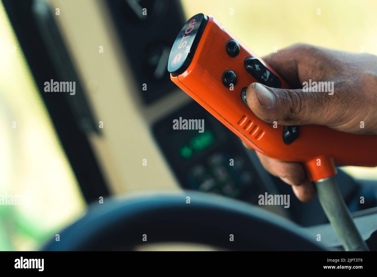 Gros plan de la télécommande rouge avec boutons noirs utilisés par les mains caucasiennes recouvertes de poussière. Opérateur de la moissonneuse-batteuse. Arrière-plan flou. Photo de haute qualité Banque D'Images
