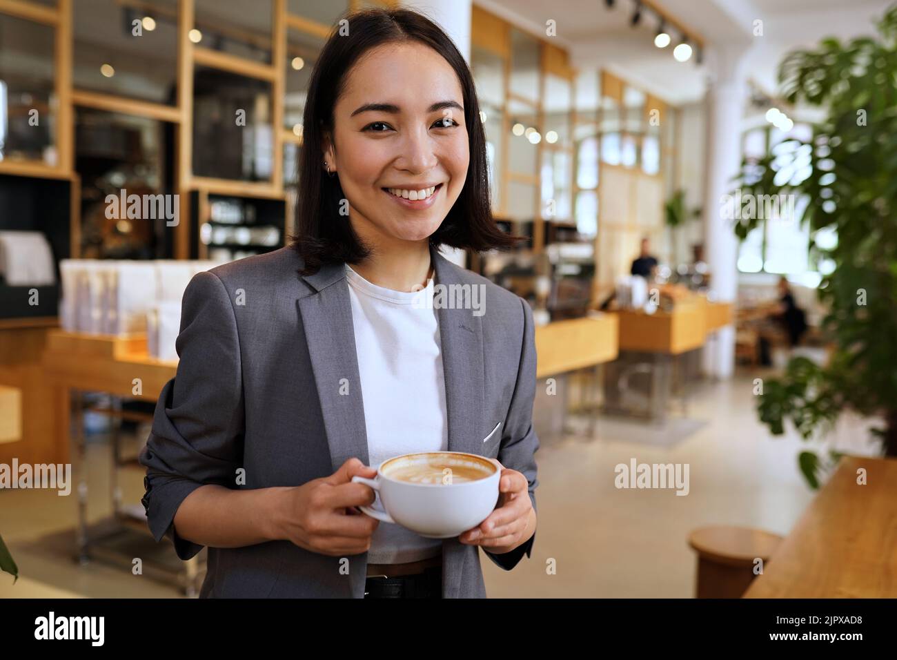 Jeune femme professionnelle asiatique souriante vêtue d'un costume tenant un café ou un portrait Banque D'Images