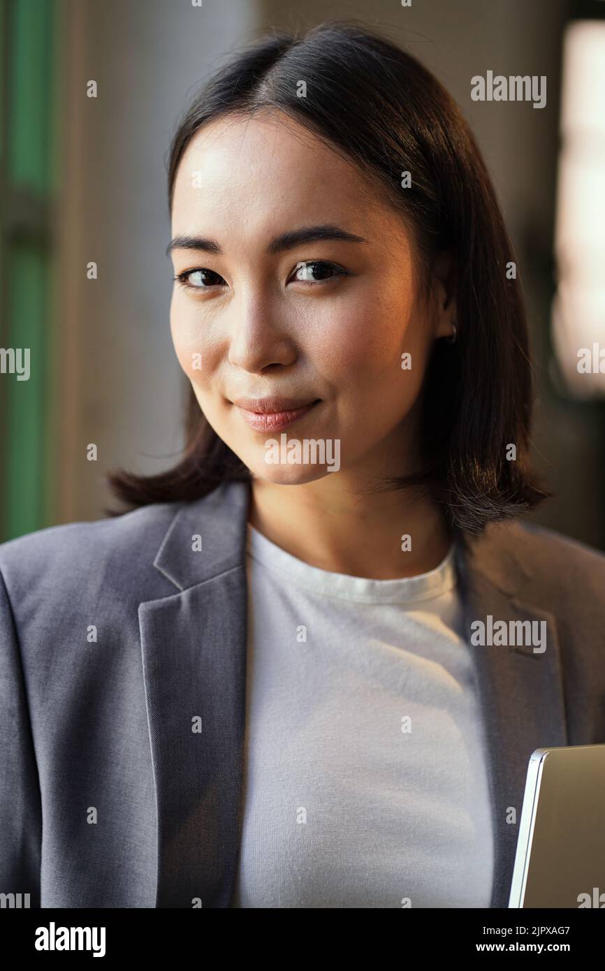 Jeune femme asiatique souriante, femme exécutive, vêtue d'un costume, portrait à la verticale. Banque D'Images