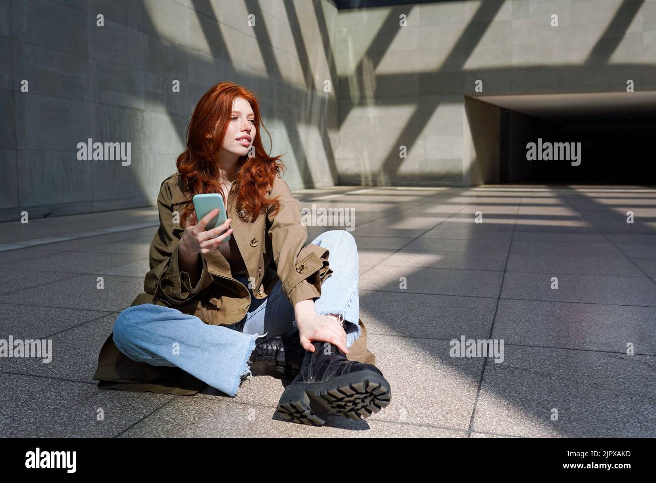REDHEAD cool adolescente en utilisant le téléphone assis sur les murs de ville urbaine arrière-plan. Banque D'Images