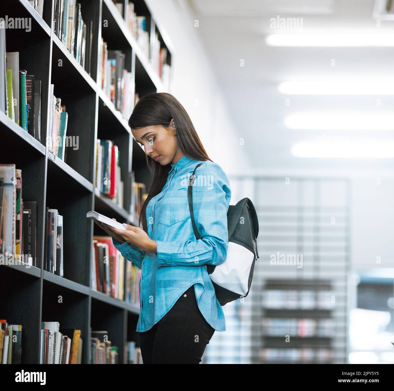 Rattraper sa longue liste de lecture. Une étudiante de l'université lisant un livre dans la bibliothèque du campus. Banque D'Images