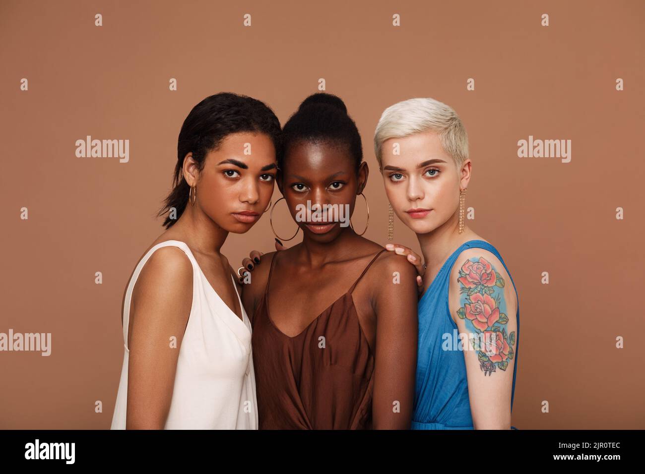 Groupe de trois femmes de différentes races debout ensemble sur fond marron Banque D'Images
