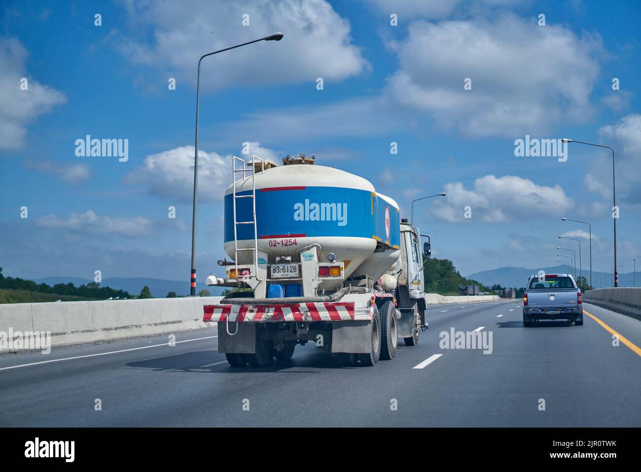 Camion de ciment de couleur bleue sur une autoroute sous un ciel bleu avec des nuages blancs. Banque D'Images