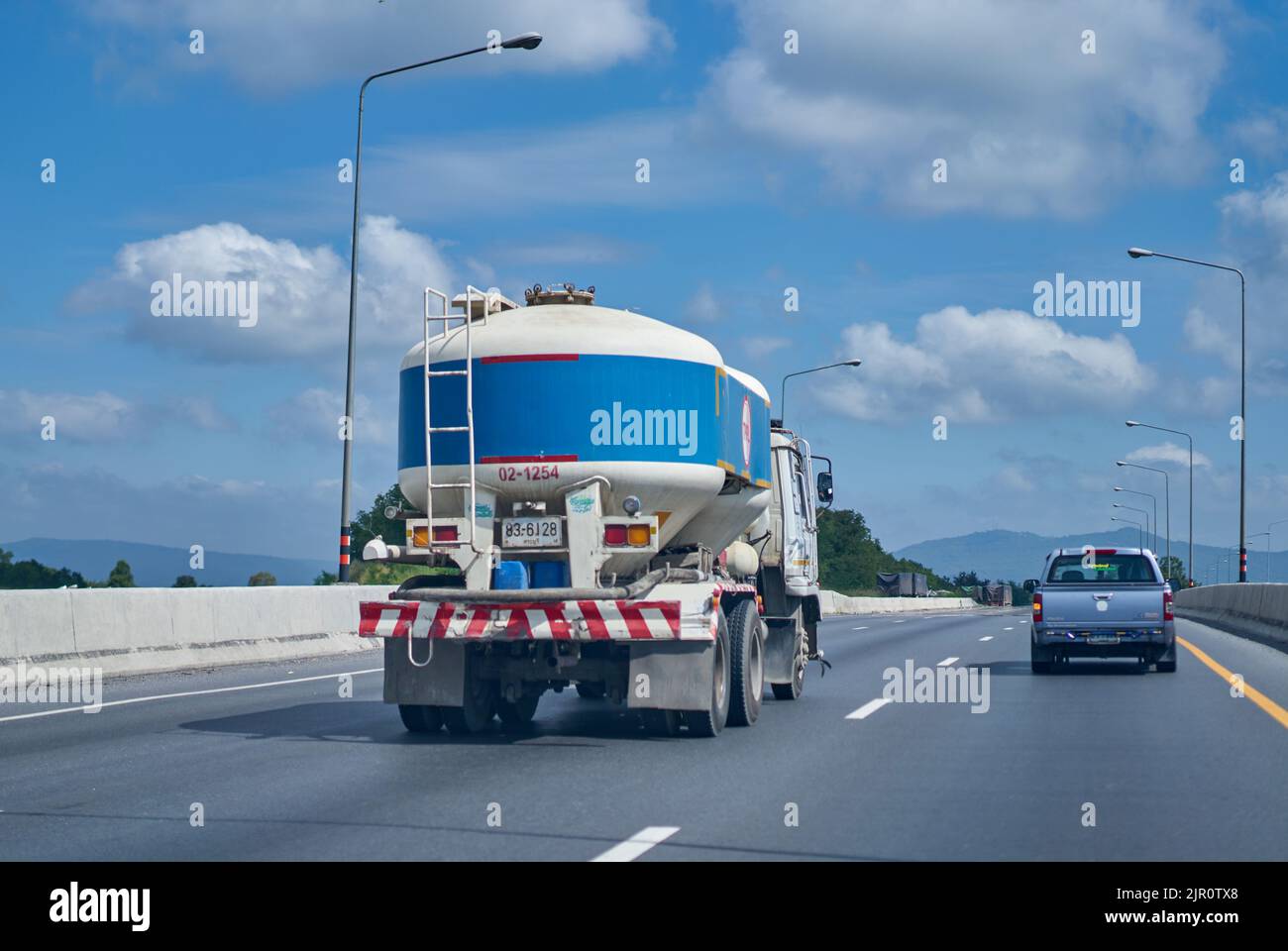 Camion de ciment de couleur bleue sur une autoroute sous un ciel bleu avec des nuages blancs. Banque D'Images
