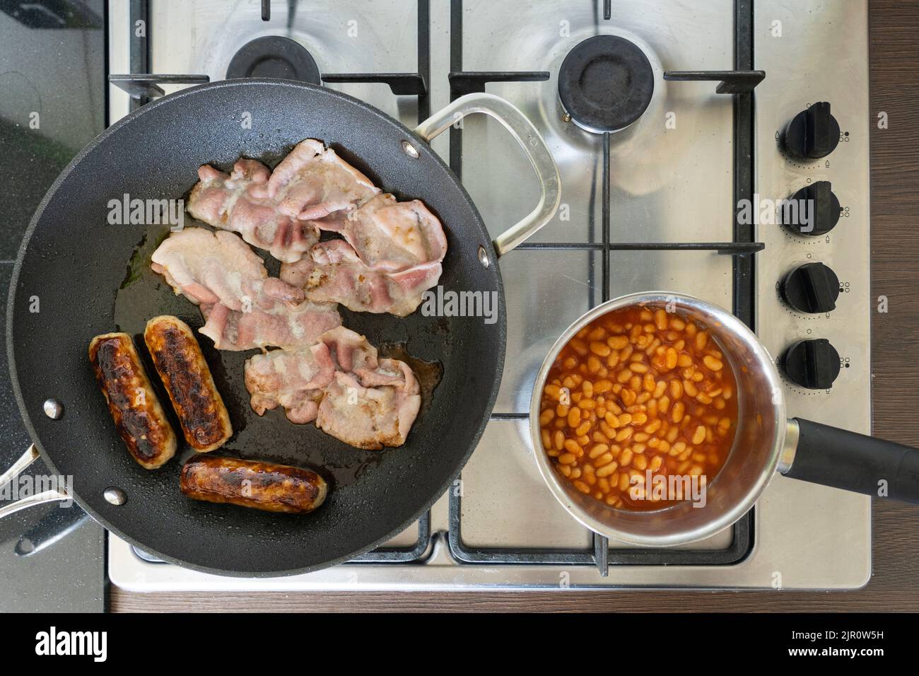 Les ingrédients traditionnels du petit-déjeuner anglais cuisent et friture sur une cuisinière à gaz. Bacon, saucisses et haricots. ROYAUME-UNI. Concept - manger malsain Banque D'Images
