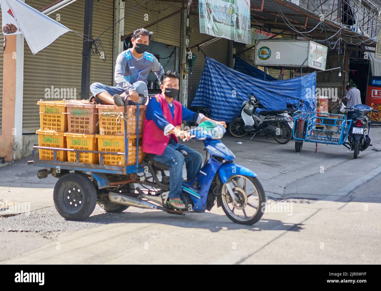 Employés sur un marché des fruits et légumes en Thaïlande, transportant des boîtes de fruits sur une moto. Banque D'Images
